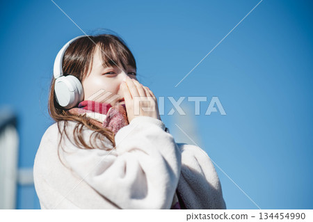 Smiling girl standing under the blue sky and listening to music Smiling girl standing under the blue sky and listening to music 134454990