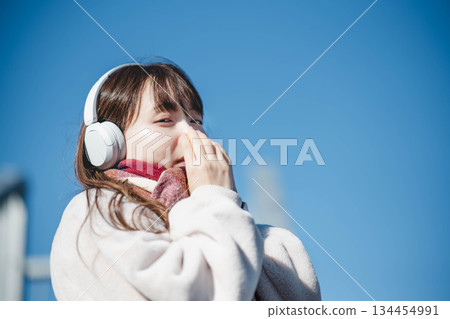一位微笑的女孩站在藍天下，聽著音樂。 134454991