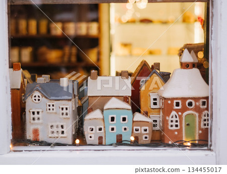 Miniature ceramic houses displayed in a shop window with warm festive lighting. 134455017