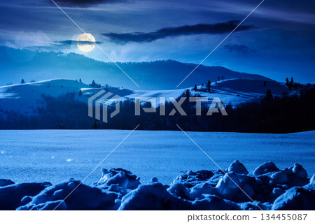 beautiful winter landscape with snow covered rolling hills under dark sky at night. majestic mountains in full moon light. frosty countryside scenery. backdrop for fiction art or mystery concepts 134455087