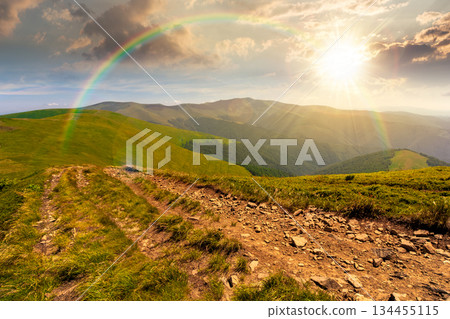 green rolling hills of mountain ridge at sunset. grassy alpine meadows and sky with clouds in evening light. summer landscape of highlands. distant peak. timeless nostalgia book cover with rainbow green rolling hills of mountain ridge at sunset. grassy alpine meadows and sky with clouds in evening light. summer landscape of highlands. distant peak. timeless nostalgia book cover with rainbow 134455115