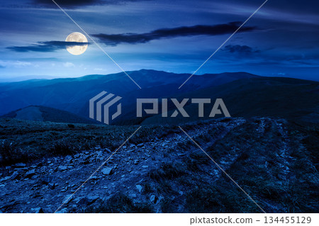 green rolling hills of mountain ridge at night. grassy alpine meadows and sky in full moon light. summer landscape of highlands. distant peak. inner strength to overcome fear, loneliness in darkness 134455129