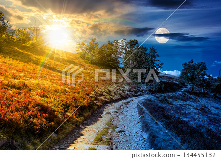 dirt gravel road winding uphill. time change concept. hiking trail in mountain landscape under sky with sun and moon. path through steep slope. uncertainty, trust issues, and difficult relationship dirt gravel road winding uphill. time change concept. hiking trail in mountain landscape under sky with sun and moon. path through steep slope. uncertainty, trust issues, and difficult relationship 134455132