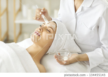 Beautician doing facial treatment and applying beauty mask on face of young woman Beautician doing facial treatment and applying beauty mask on face of young woman 134455143