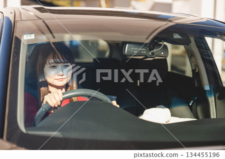 在陽光明媚的日子裡,一位留著長髮的年輕女子開車。 在陽光明媚的日子裡,一位留著長髮的年輕女子開車。 134455196