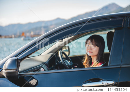 在陽光明媚的日子裡,一位留著長髮的年輕女子開車。 在陽光明媚的日子裡,一位留著長髮的年輕女子開車。 134455204