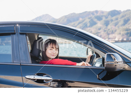A young long-haired woman driving a car on a sunny day 134455229