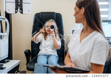 Sitting and holding notepad. Little girl at the ophthalmologist clinic with doctor 134455377