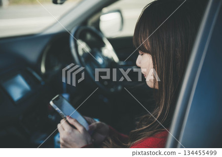 A young woman operating a smartphone in the passenger seat A young woman operating a smartphone in the passenger seat 134455499