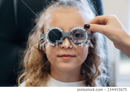 Portrait, in glasses, looking forward. Little girl at the ophthalmologist clinic with doctor 134455675