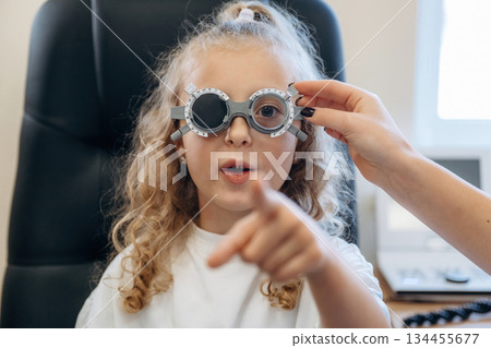 Portrait, in glasses, looking forward. Little girl at the ophthalmologist clinic with doctor Portrait, in glasses, looking forward. Little girl at the ophthalmologist clinic with doctor 134455677