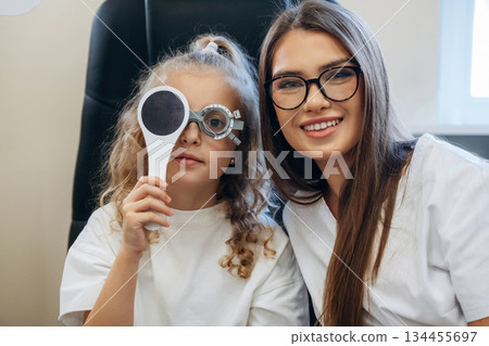 Helping, covering the eye. Little girl at the ophthalmologist clinic with doctor Helping, covering the eye. Little girl at the ophthalmologist clinic with doctor 134455697