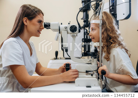 View from the side. Little girl at the ophthalmologist clinic with doctor View from the side. Little girl at the ophthalmologist clinic with doctor 134455712