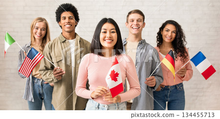 Young students of language school celebrate holiday. Happy millennial peoples of different nationalities have fun on study and hold little flags on brick white wall background, studio shot, free space 134455713