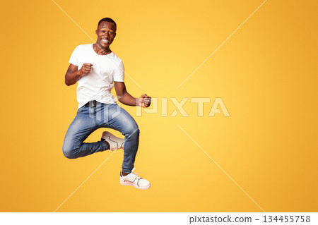 Cute black guy jumping up in the air and showing funny figures, having good day, showing positive emotions over orange background. African american man posing at studio, having fun 134455758