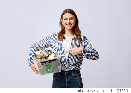 Metal Recycle. Positive Millennial Lady Holding And Pointing At Plastic Container With Aluminum Cans, Young Eco-Activist Woman Enjoying Waste Sorting System, Standing On Light Background, Free Space Metal Recycle. Positive Millennial Lady Holding And Pointing At Plastic Container With Aluminum Cans, Young Eco-Activist Woman Enjoying Waste Sorting System, Standing On Light Background, Free Space 134455814