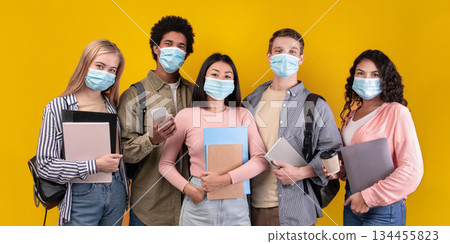 Study abroad and student exchange during covid-19 lockdown. Modern cheerful teens multiracial students with notepads, gadgets, cups of coffee looking at camera, isolated on orange background 134455823