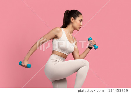Training Concept. Full Length Portrait Of Confident Fit Young Lady In Sportswear Exercising With Two Dumbbells And Lifting Leg Up, Isolated On Pink Studio Background. Energy And Sports 134455839