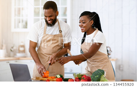 Happy African American Spouses Using Laptop Computer While Cooking In Kitchen Together, Searching Recipe In Internet, Smiling Black Couple Preparing Healthy Food For Dinner At Home, Copy Space Happy African American Spouses Using Laptop Computer While Cooking In Kitchen Together, Searching Recipe In Internet, Smiling Black Couple Preparing Healthy Food For Dinner At Home, Copy Space 134455920