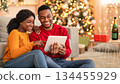 Home cozy in New Year and Christmas and video call to friends or family. Happy millennial african american lovers guy and lady talking on digital tablet in living room interior with tree with garlands 134455929