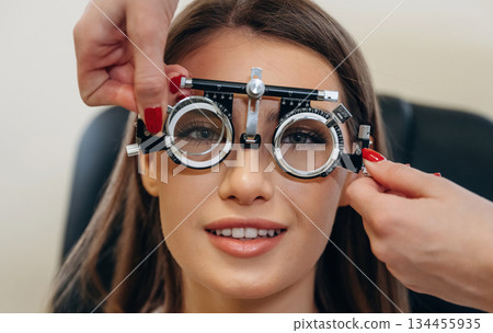 Positive facial expression. Young woman is checking her vision in the ophthalmologist cabinet Positive facial expression. Young woman is checking her vision in the ophthalmologist cabinet 134455935