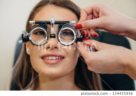 Positive facial expression. Young woman is checking her vision in the ophthalmologist cabinet Positive facial expression. Young woman is checking her vision in the ophthalmologist cabinet 134455936
