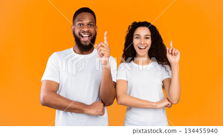 Multiracial Couple Pointing Fingers Up Having Great Idea Posing Over Yellow Studio Background, Smiling To Camera. Eureka Moment, Inspiration, Great Solution Concept. Panorama 134455940