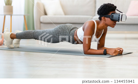 VR Workout. Black Fitness Lady Standing In Plank Wearing VR Headset Exercising During Training In Virtual Gym At Home. Augmented Reality Application For Smart Sport. Side View 134455941