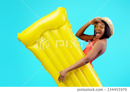 Millennial black woman in swimsuit holding yellow inflatable lilo on blue studio background. Young African American lady with pool float having tropical summer vacation or beach party 134455970