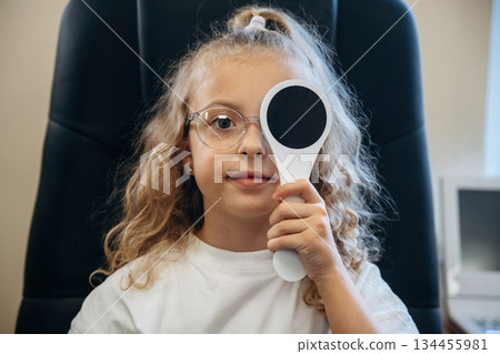 Session of testing the sight sharpness. Little girl is checking vision in the ophthalmologist cabinet Session of testing the sight sharpness. Little girl is checking vision in the ophthalmologist cabinet 134455981