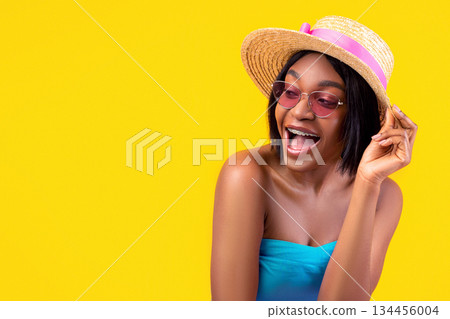 Flirty young black woman in summertime outfit opening mouth in excitement, posing on orange studio background. Playful African American lady looking forward to summer vacation 134456004