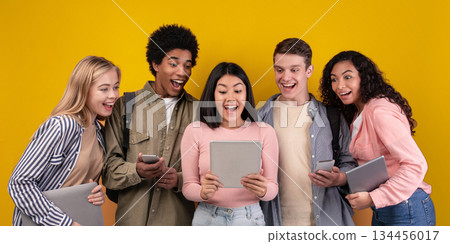 Modern gadgets, social networks and education. Shocked cheerful young multi ethnic students looking in digital tablet in asian female hands, with open mouths, isolated on orange background, copy space 134456017