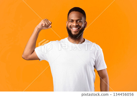 Strength Concept. Cheerful Black Guy Showing Biceps Muscles Posing Standing On Yellow Background In Studio, Smiling To Camera. Gym Advertisement Banner, Male Power Concept 134456056