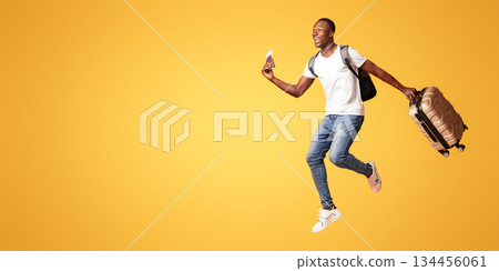Finally vacation. Young happy black man with suitcase, backpack, passport and flight tickets jumping up orange studio background. Excited african american guy running towards copy space, panorama Finally vacation. Young happy black man with suitcase, backpack, passport and flight tickets jumping up orange studio background. Excited african american guy running towards copy space, panorama 134456061