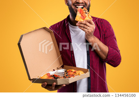 Happy African Man Eating Pizza Smiling To Camera Standing Over Yellow Studio Background. Junk Food Eater Enjoying Unhealthy Pizza. Nutrition And Cheat Meal, Fastfood Overeating Habit Happy African Man Eating Pizza Smiling To Camera Standing Over Yellow Studio Background. Junk Food Eater Enjoying Unhealthy Pizza. Nutrition And Cheat Meal, Fastfood Overeating Habit 134456100