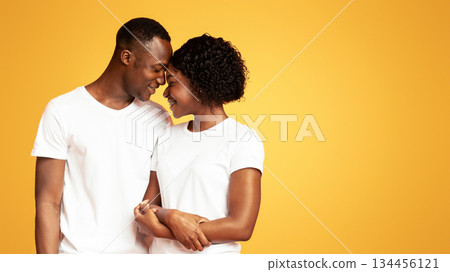 Closeup of loving black couple attractive young man and woman in jeans and white t-shirts bonding on orange studio background, cuddling and smiling, copy space. Love, family, relationships concept Closeup of loving black couple attractive young man and woman in jeans and white t-shirts bonding on orange studio background, cuddling and smiling, copy space. Love, family, relationships concept 134456121