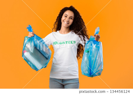Sort Your Waste. Volunteer Lady Holding Blue Plastic Garbage Bags Posing Smiling To Camera Standing In Studio Over Yellow Background. Litter And Trash Sorting, Clean Environment Concept Sort Your Waste. Volunteer Lady Holding Blue Plastic Garbage Bags Posing Smiling To Camera Standing In Studio Over Yellow Background. Litter And Trash Sorting, Clean Environment Concept 134456124