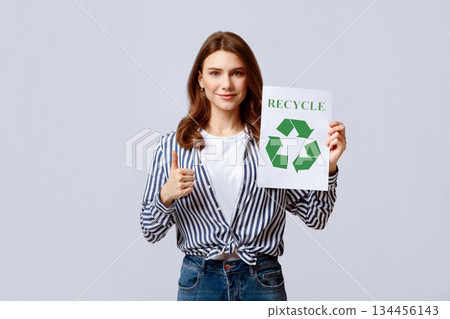 Young Eco-Activist Demonstrating Motivational Placard With Recycle Sign And Showing Thumb Up, Millennial Woman Promoting Zero Waste Living, Standing On Grey Studio Background, Free Space Young Eco-Activist Demonstrating Motivational Placard With Recycle Sign And Showing Thumb Up, Millennial Woman Promoting Zero Waste Living, Standing On Grey Studio Background, Free Space 134456143