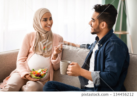 Dometic Leisure. Pregnant Muslim Lady In Hijab Eating Fresh Vegetable Salad While Husband Drinking Coffee At Home, Happy Expectant Middle Eastern Spouses Relaxing Together On Couch In Living Room Dometic Leisure. Pregnant Muslim Lady In Hijab Eating Fresh Vegetable Salad While Husband Drinking Coffee At Home, Happy Expectant Middle Eastern Spouses Relaxing Together On Couch In Living Room 134456212