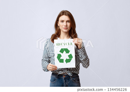 Recycling Concept. Young Beautiful Lady Demonstrating Placard With Green Recycle Sign, Millennial Eco-Friendly Nature-Lover Woman Standing Over Grey Studio Background, Looking At Camera, Copy Space 134456226