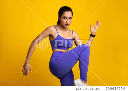 Aerobics Sport Exercises And Healthy Lifestyle. Portrait Of Determined Slim Young Lady Lifting Leg Up, Doing High Knees Cardio Exercise Looking At Camera Isolated On Orange Studio Background 134456234