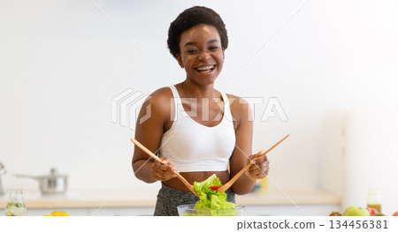 Healthy Diet. African Lady Cooking Salad Slimming At Home, Posing Wearing Fitwear Standing In Modern Kitchen Indoors, Smiling To Camera. Weight Loss Nutrition And Dieting Concept Healthy Diet. African Lady Cooking Salad Slimming At Home, Posing Wearing Fitwear Standing In Modern Kitchen Indoors, Smiling To Camera. Weight Loss Nutrition And Dieting Concept 134456381