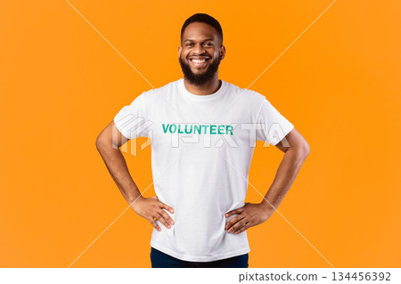 Cheerful African Volunteer Guy Standing With His Hands On Hips Ready For Voluntary Work Posing On Yellow Studio Background, Smiling To Camera. Volunteering Job, Activist's Portrait Concept 134456392
