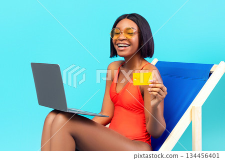 Happy African American lady using laptop in lounge chair, showing credit card, shopping online on blue studio background. Joyful black woman buying goods in web store on summer sale Happy African American lady using laptop in lounge chair, showing credit card, shopping online on blue studio background. Joyful black woman buying goods in web store on summer sale 134456401