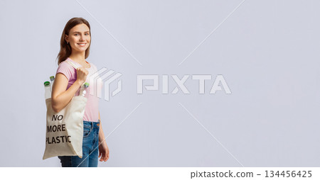 Smiling Young Woman Carrying Eco Tote Bag With No More Plastic Inscription Filled With Empty Bottles Ready For Recycling, Millennial Lady Walking Over Light Studio Background, Copy Space Smiling Young Woman Carrying Eco Tote Bag With No More Plastic Inscription Filled With Empty Bottles Ready For Recycling, Millennial Lady Walking Over Light Studio Background, Copy Space 134456425
