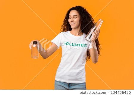No More Plastic. Female Volunteer Choosing Between Glass And Plastic Bottle Posing Standing In Studio Over Yellow Background. Stop Using Single-Used Bottles, Ecology Concept No More Plastic. Female Volunteer Choosing Between Glass And Plastic Bottle Posing Standing In Studio Over Yellow Background. Stop Using Single-Used Bottles, Ecology Concept 134456430