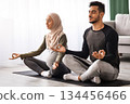 Expecting Muslim Spouses Practicing Yoga Together At Home, Sitting In Lotus Pose With Closed Eyes On Mat In Living Room, Calm Islamic Couple Enjoying Healthy Lifestyle During Pregnancy, Free Space 134456466