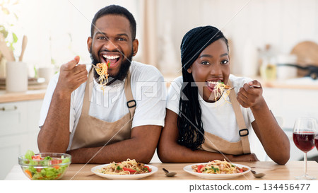 Cheerful Black Spouses Sitting At Table Eating Tasty Lunch In Kitchen, Happy African American Couple Having Spaghetti And Vegetable Salad, Enjoying Delicious Food While Spending Time At Home, Closeup 134456477