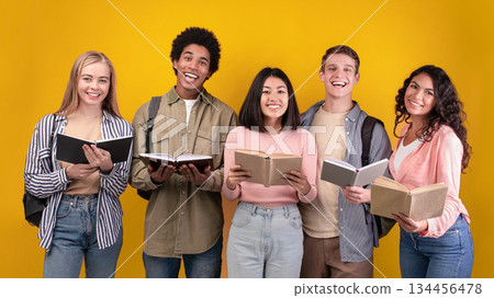 Modern and collaborative learning, knowledge sharing, happiness group of people. Smiling young multi ethnic students read books and notes, isolated on orange background, copy space, studio shot 134456478