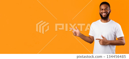 African Guy Pointing Fingers Aside Standing Over Yellow Studio Background, Smiling To Camera, Advertising Your Text. Look There, Advertisement Banner. Panorama, Blank Space African Guy Pointing Fingers Aside Standing Over Yellow Studio Background, Smiling To Camera, Advertising Your Text. Look There, Advertisement Banner. Panorama, Blank Space 134456485